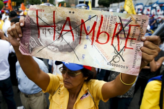 Một người phụ nữ Venezuela ghi chữ "Đói" trên tờ tiền 100 bolivar trong cuộc biểu tình phản đối chính phủ tháng 8.2015 (Ảnh: Internet).