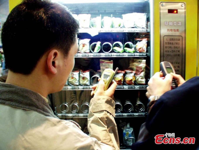 Hình ảnh một người đàn ông mua đồ ăn tại siêu thị bằng một chiếc điện thoại di động vào năm 2001. Khái niệm mua hàng bằng máy bán hàng tự động GSM trở nên khá phổ biến tại tỉnh Phúc Châu, Trung Quốc. Khách hàng có thể mua đồ ăn bằng cách soạn cú pháp tin nhắn và tiền sẽ được trừ trực tiếp vào tài khoản.