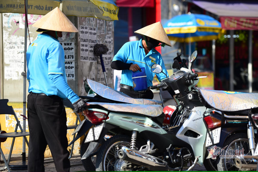 Nhân viên một cửa hàng dùng tấm bạc che yên xe máy tránh nóng cho khách hàng