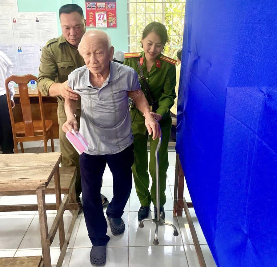 Cán bộ Công an xã Phan Ngọc Hiển cùng lực lượng an ninh, trật tự cơ sở hỗ trợ cụ ông Lư Văn Tý thực hiện bỏ phiếu.