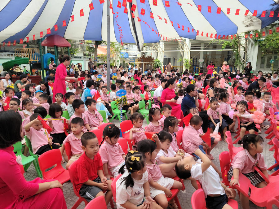 Sân trường ngập tràn sắc màu tươi vui, rộn rã với sự đan xen giữa đồng phục hồng của các bé và tà áo dài đỏ thắm của các cô giáo. Dù xen lẫn đôi chút hiếu động, tinh nghịch vốn có của trẻ nhỏ, không gian chung vẫn toát lên tinh thần hân hoan, rạo rực đón chào năm học mới.