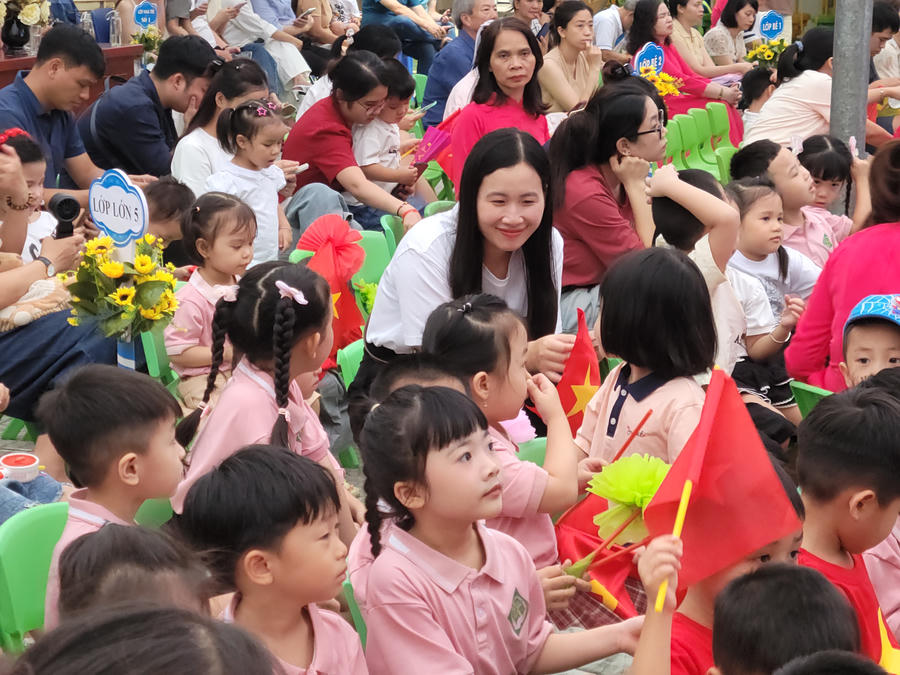 Nụ cười hiền hậu của phụ huynh khi ân cần trò chuyện cùng các bé lớp Lớn 5 mang đến bầu không khí thật dịu dàng, đong đầy yêu thương. Khoảnh khắc những ánh mắt ngây thơ, tròn xoe hướng về phía trước với lá cờ đỏ trên tay đã khắc họa trọn vẹn nét trong trẻo, bỡ ngỡ đáng yêu của lứa tuổi mầm non.