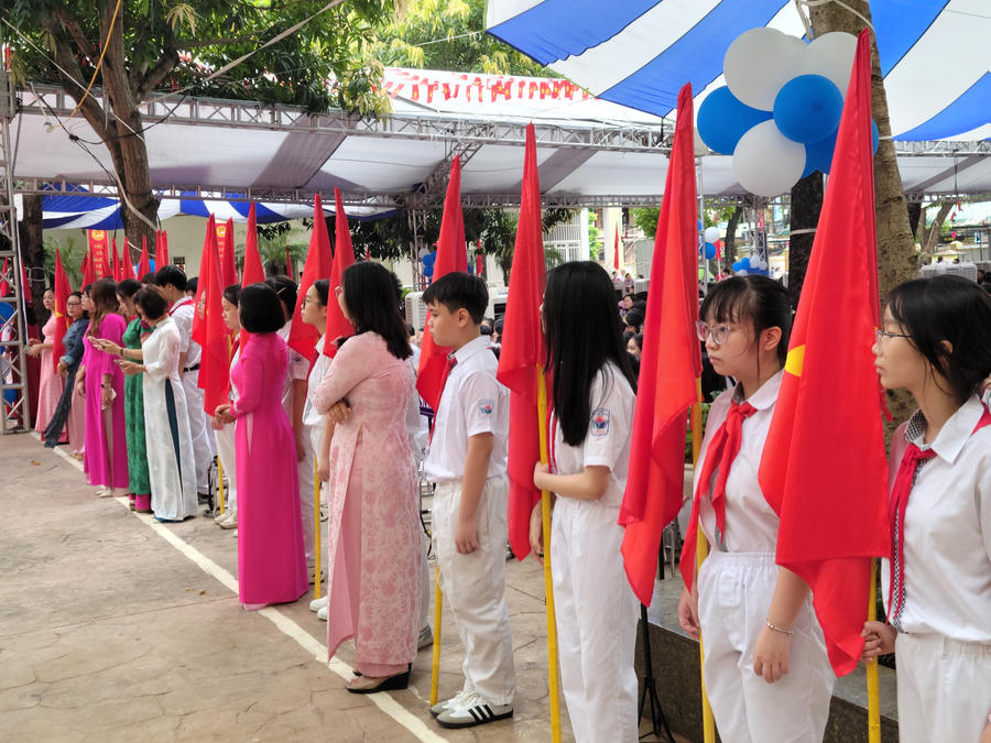Dưới bóng cây xanh mát, sắc đỏ của cờ Tổ quốc rực rỡ trên tay các em học sinh và cô giáo, tô đậm thêm vẻ trang nghiêm cho ngày hội toàn dân đưa trẻ đến trường.
