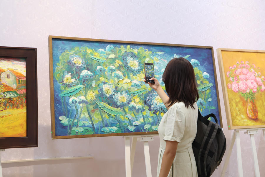 Một kh&aacute;ch tham quan d&ugrave;ng điện thoại ghi lại h&igrave;nh ảnh t&aacute;c phẩm hội họa lấy cảm hứng từ hoa sen tại triển l&atilde;m.